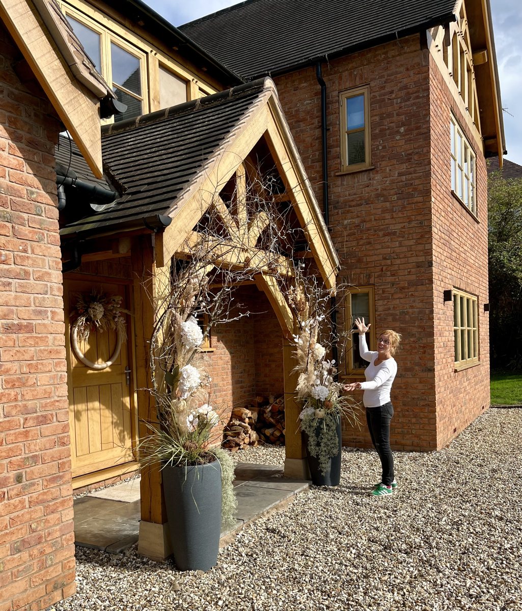 Claire beside a timber entrance decorated with branches, white flowers and tall planters.